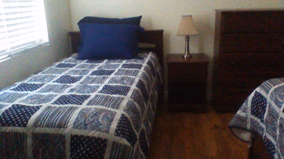 Bedroom with two twin beds covered in blue patterned quilts, a nightstand with a lamp, and a dresser.