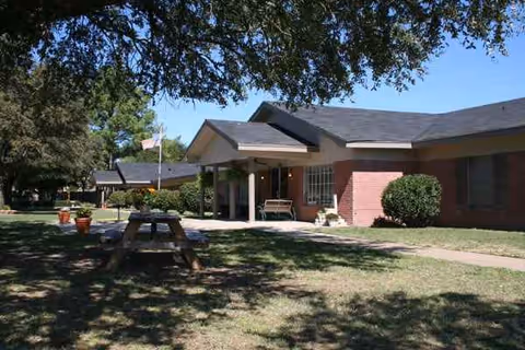 Exterior view of Groesbeck LTC Nursing-Rehab with brick building, front entrance, and picnic table.