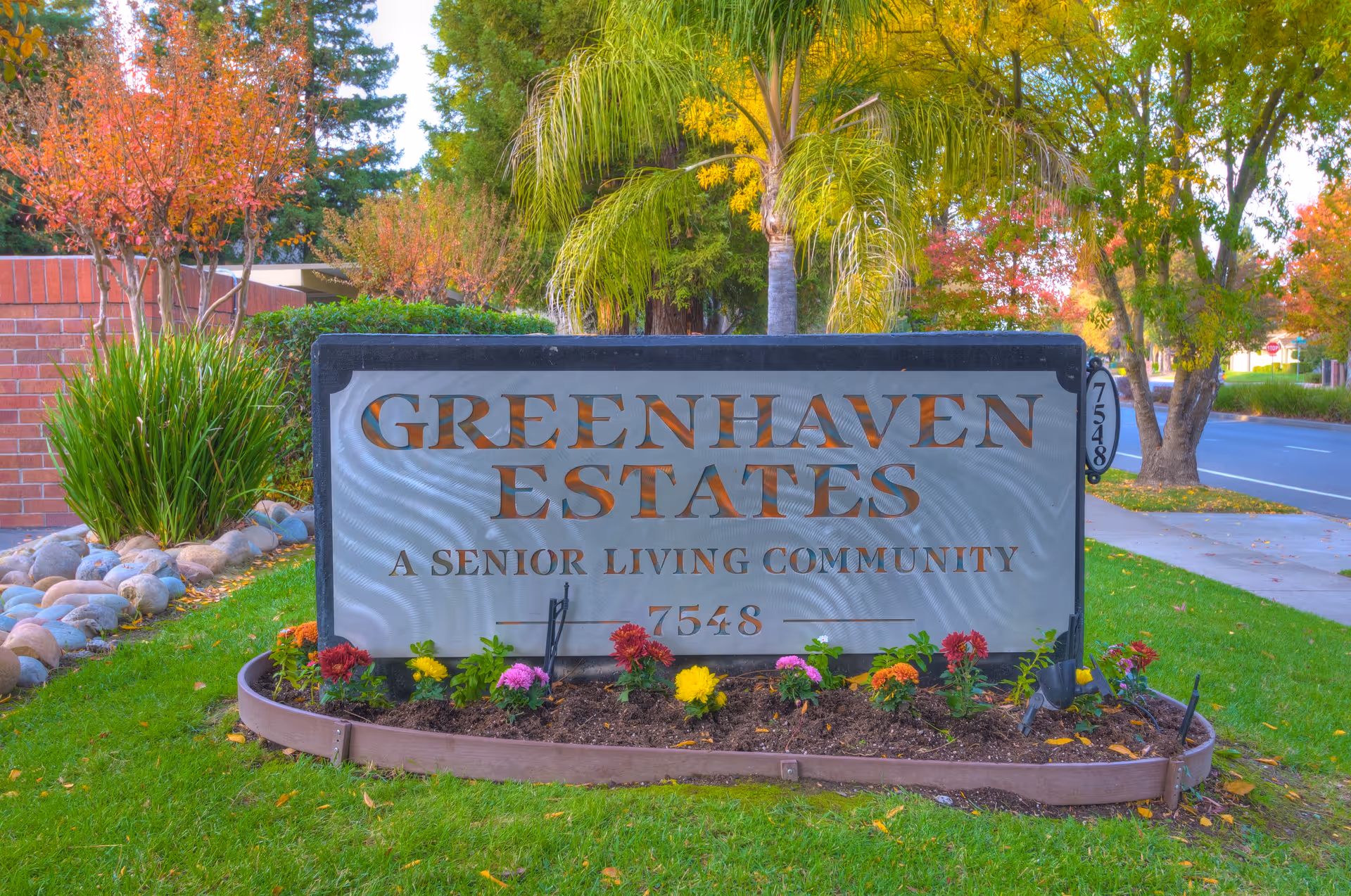 A landscaped entrance sign reading "Greenhaven Estates — A Senior Living Community" surrounded by flowers and trees.