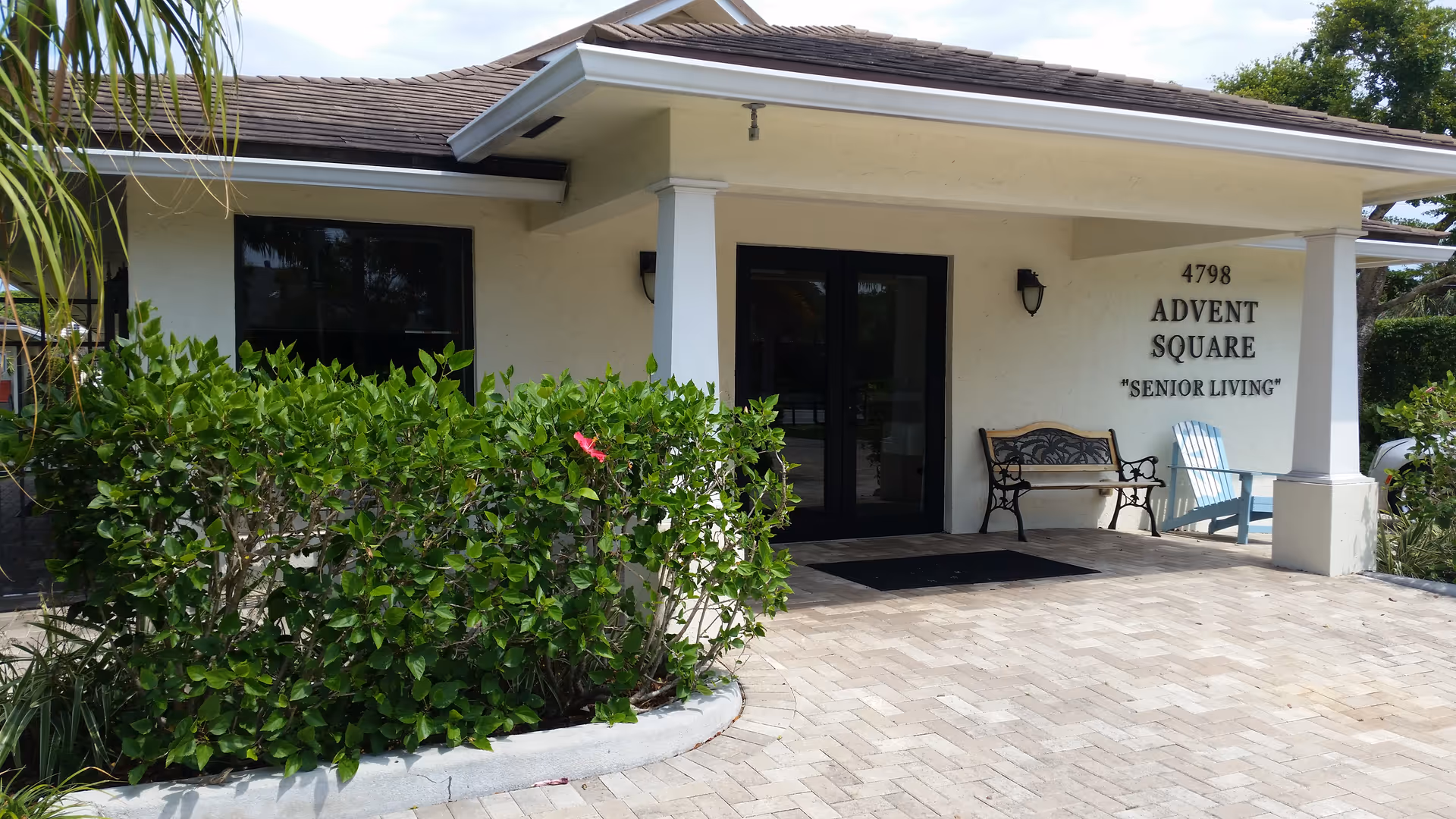 Front entrance of Advent Square Senior Living with double glass doors, benches, and hedges.
