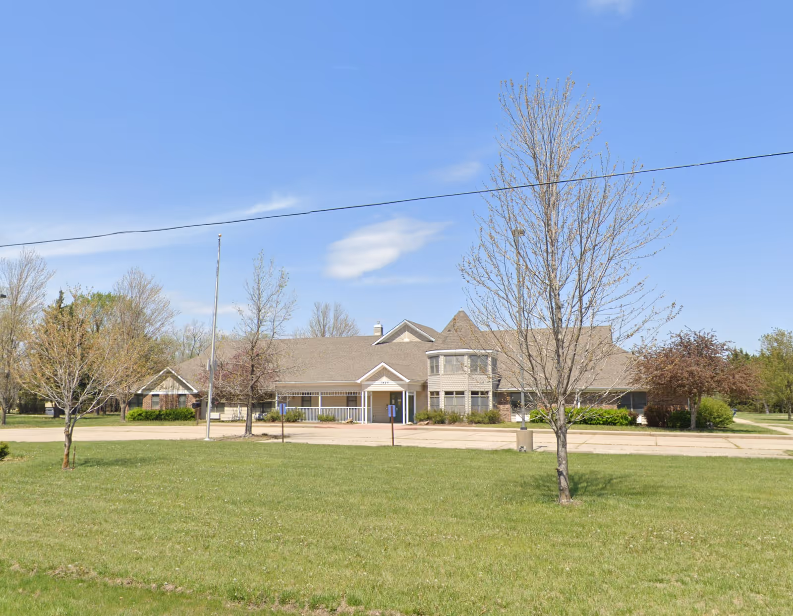 Exterior view of a single-story building with a peaked roof and a turret-like feature, surrounded by a grassy lawn and several leafless trees under a clear blue sky.