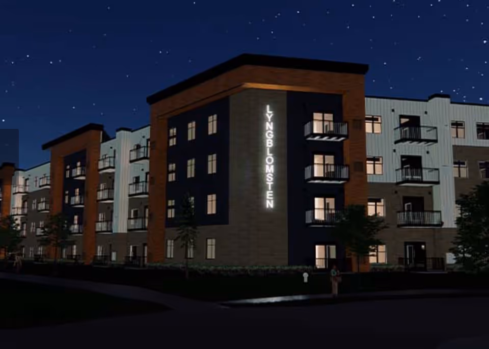 Nighttime exterior view of a multi-story senior living building with a vertical illuminated "LYNGBLOMSTEN" sign and balconies.