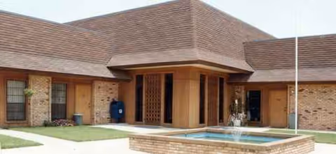 Front view of a beige-brick senior living facility entrance with a rectangular fountain