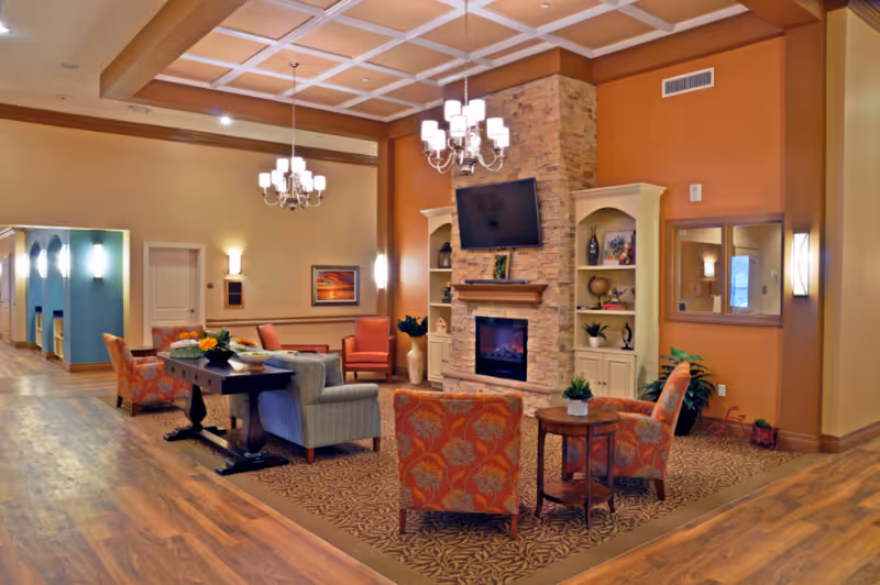 Warm senior living room with fireplace, chandeliers, built-in shelves, and comfortable seating.