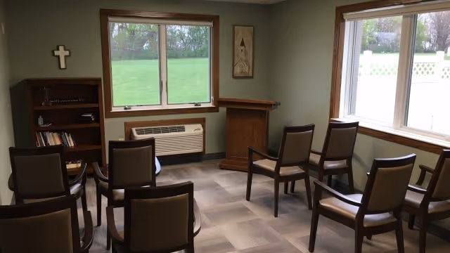 Small meeting room in a senior facility with chairs, a podium, and a cross.
