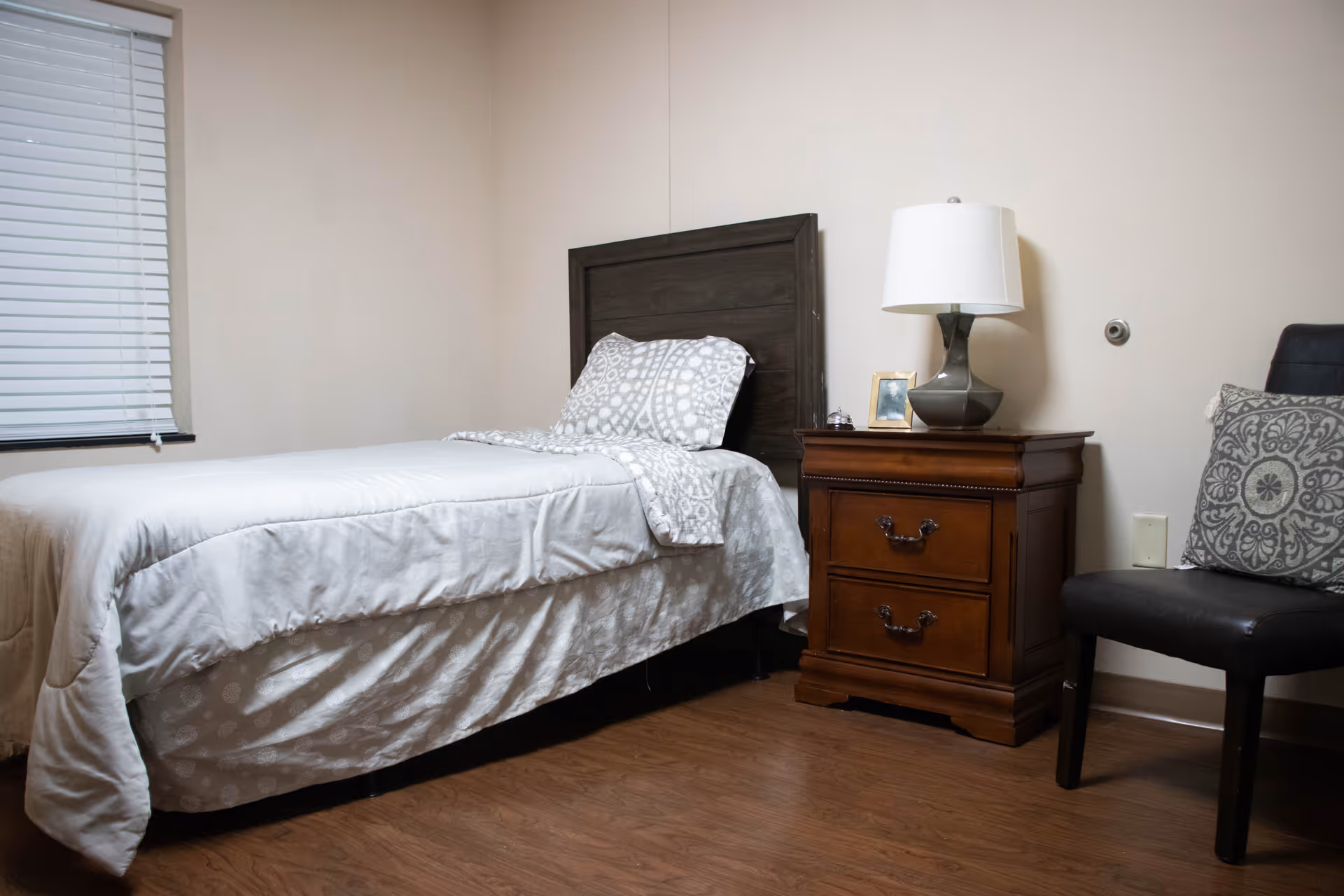 Small bedroom with a single bed, wooden headboard, a nightstand with a lamp, and a chair.