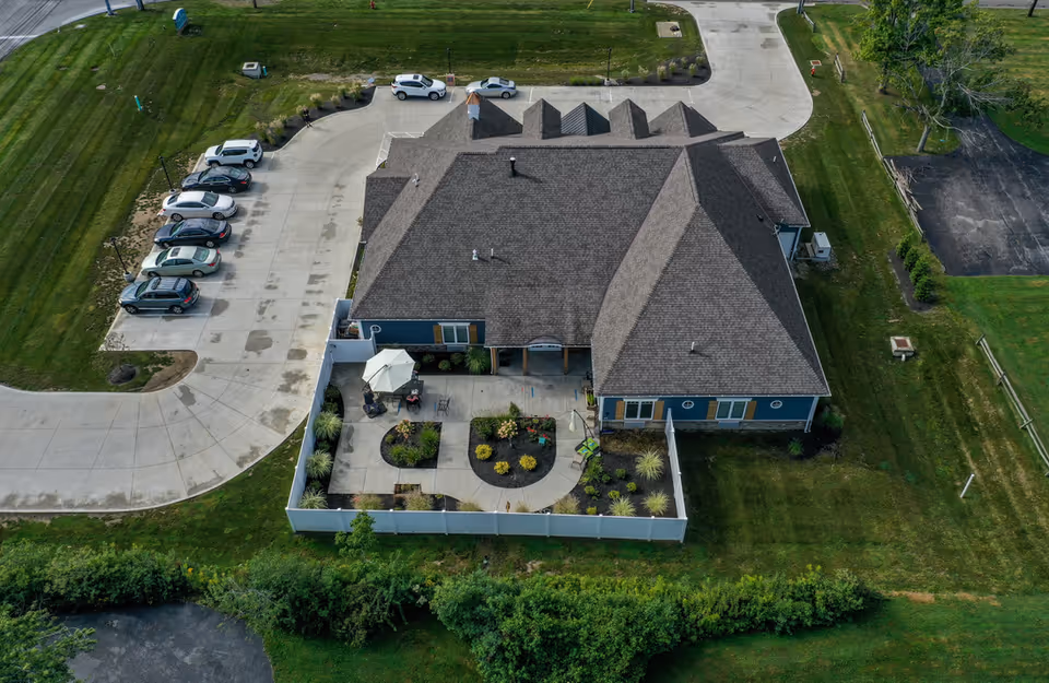 Aerial view of a single-story building with a fenced courtyard patio, nearby parking lot, and surrounding green lawn.