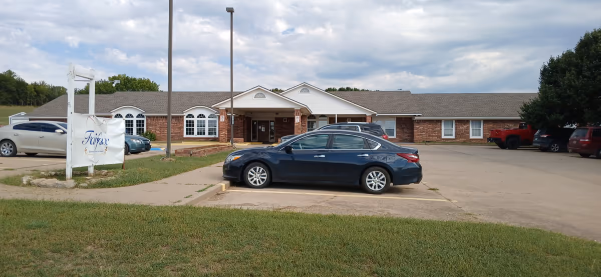 Front exterior of a single-story brick senior living facility with parked cars and a 'Fairfax' sign on a grassy lot.