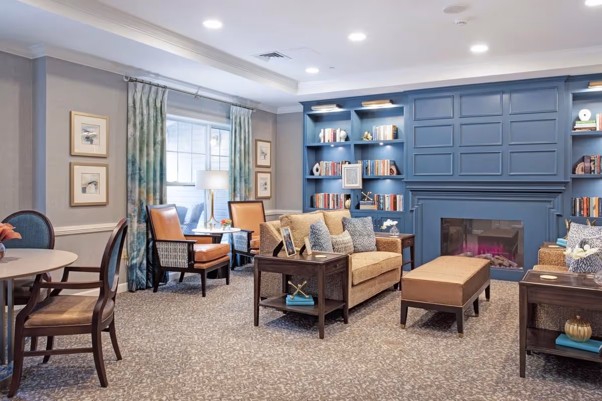 Bright, well-appointed common living room with sofas, armchairs, built-in blue bookshelves and a fireplace.