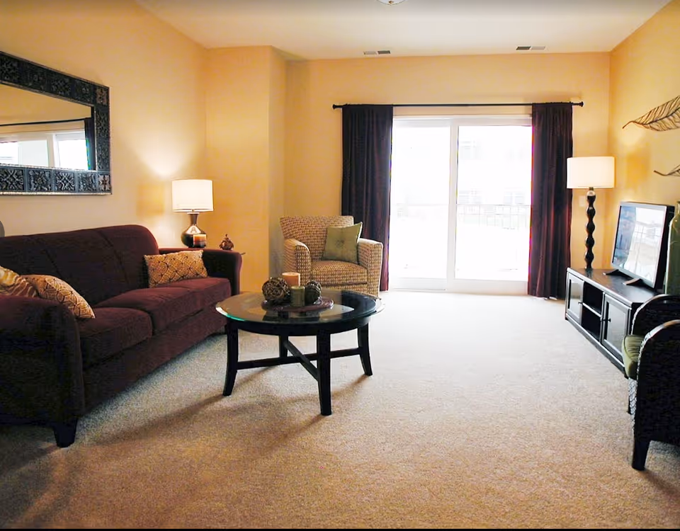 Living room with a dark red sofa, armchair, round coffee table, TV on a stand, and large sliding glass doors.