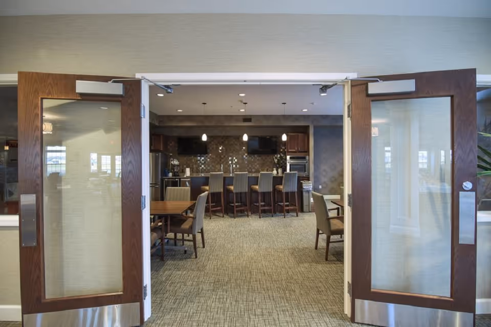 Open double doors leading into a communal dining and kitchen area with tables, chairs, and a bar with stools.