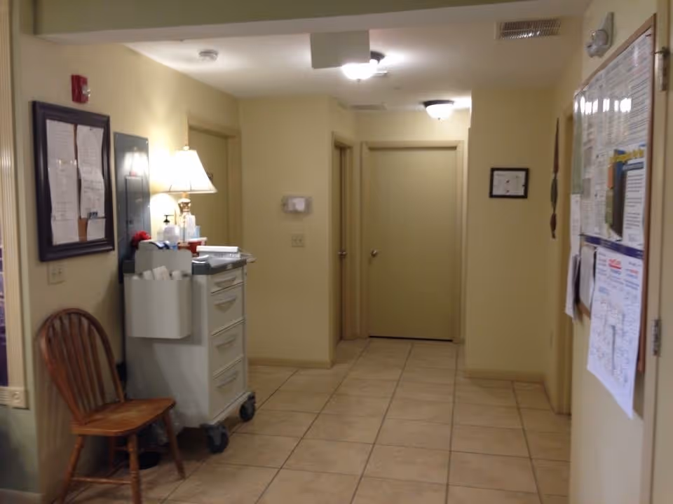 Beige-tiled interior hallway with closed doors, a rolling cart and wooden chair, and bulletin boards on the walls.