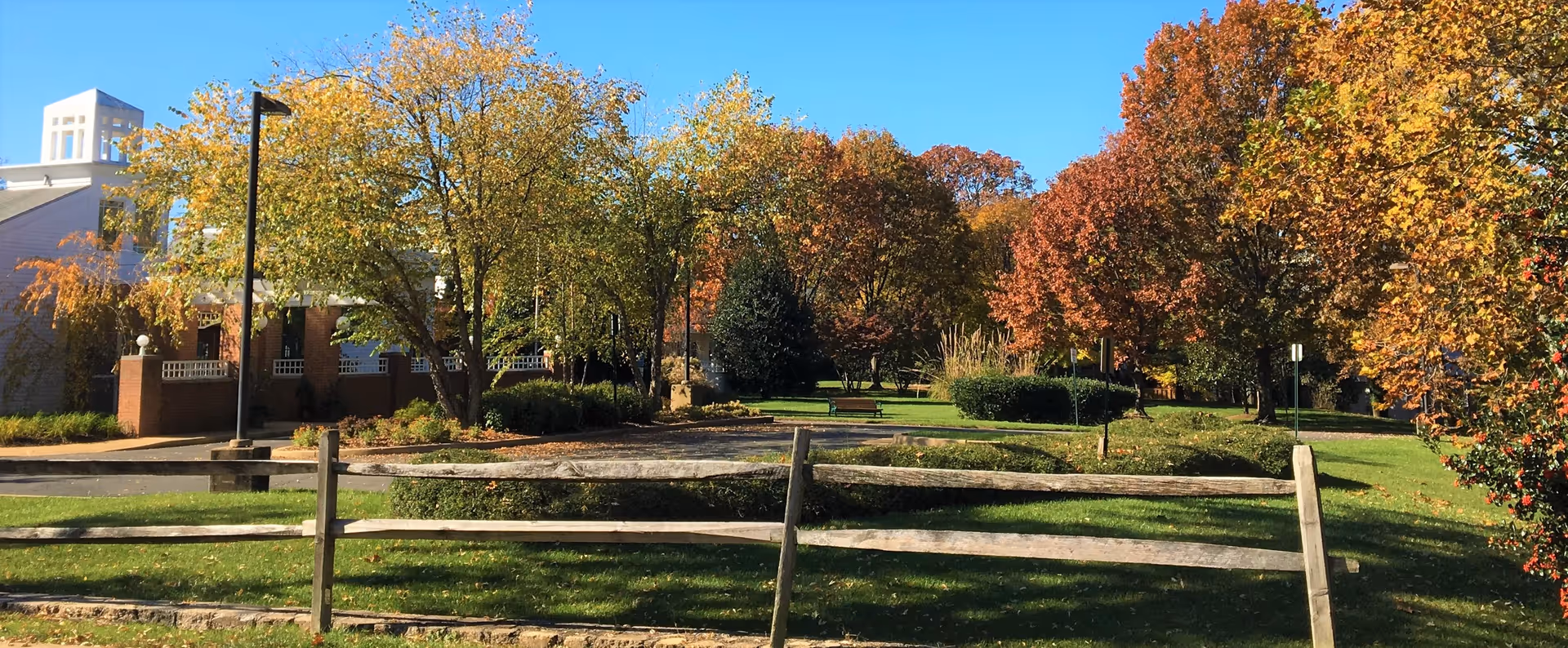 Front exterior grounds with a wooden split-rail fence, autumn trees, and a building partially visible on the left.