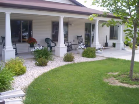 Front porch of a senior living facility with chairs, planters, and a green lawn.
