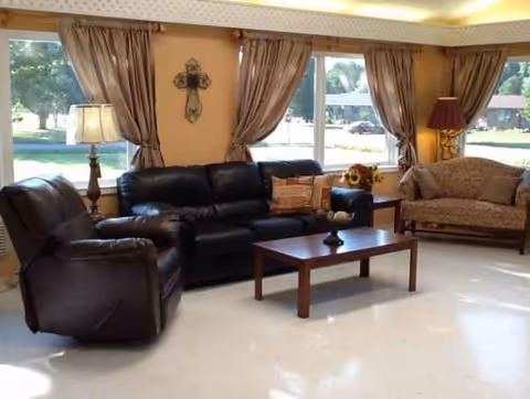 Living room in a senior facility with leather seating, a coffee table, and large windows.