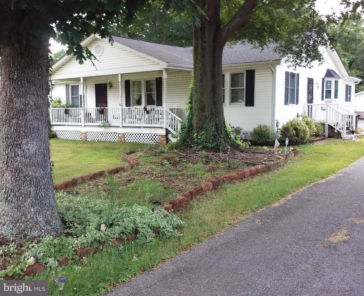 Single-story white house with a front porch, large trees, and a paved driveway.