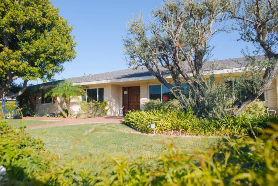 Front exterior of a single-story assisted living home with a lawn, walkway, and trees.