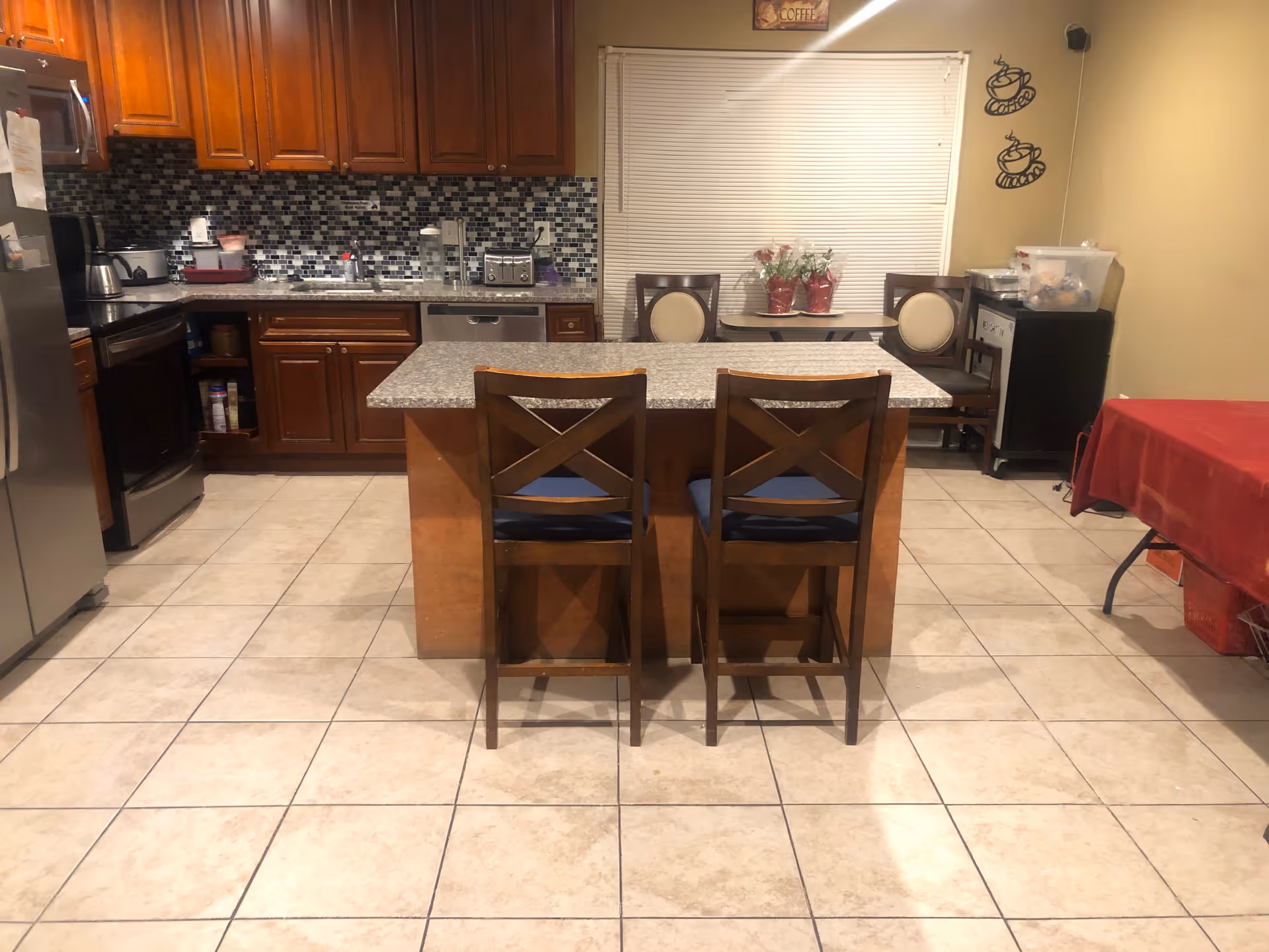 Kitchen with a center island and two bar stools, tile floor, wooden cabinets, and stainless appliances.
