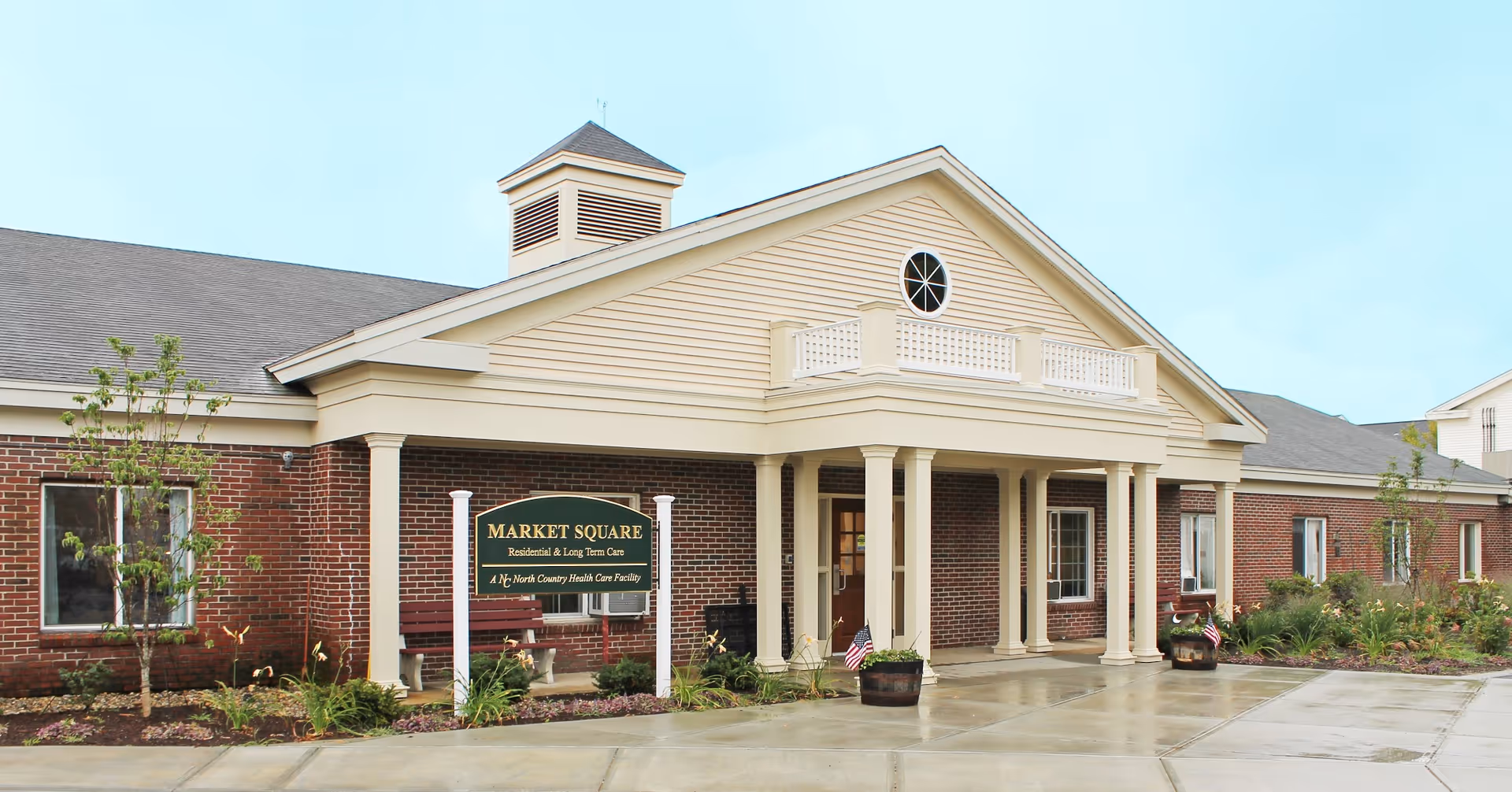 Front entrance of a single-story brick senior living facility with a covered portico, sign reading Market Square, and surrounding landscaping.