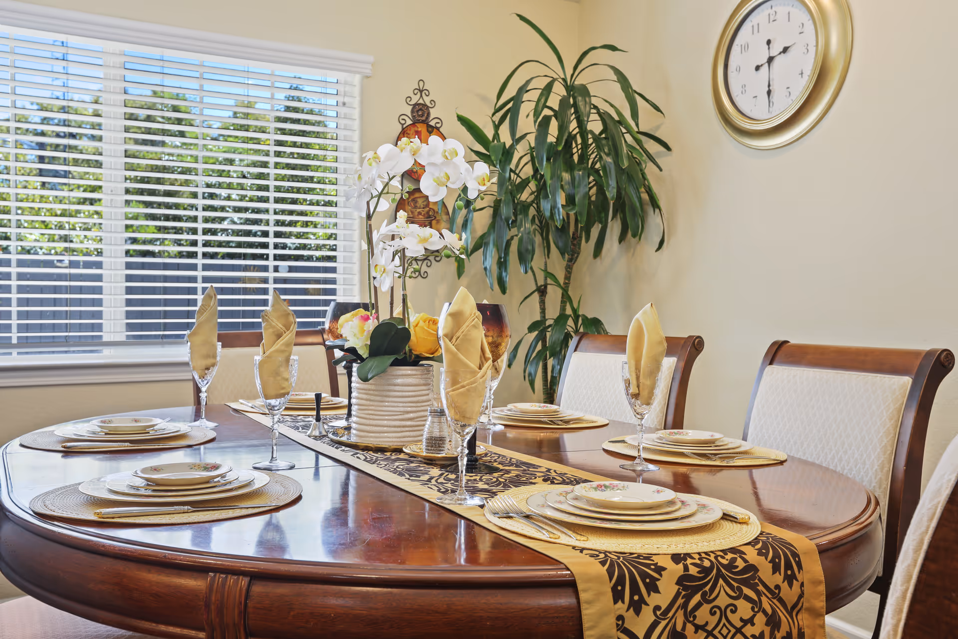 Dining room with a wooden table set for six, a floral centerpiece, and a wall clock.