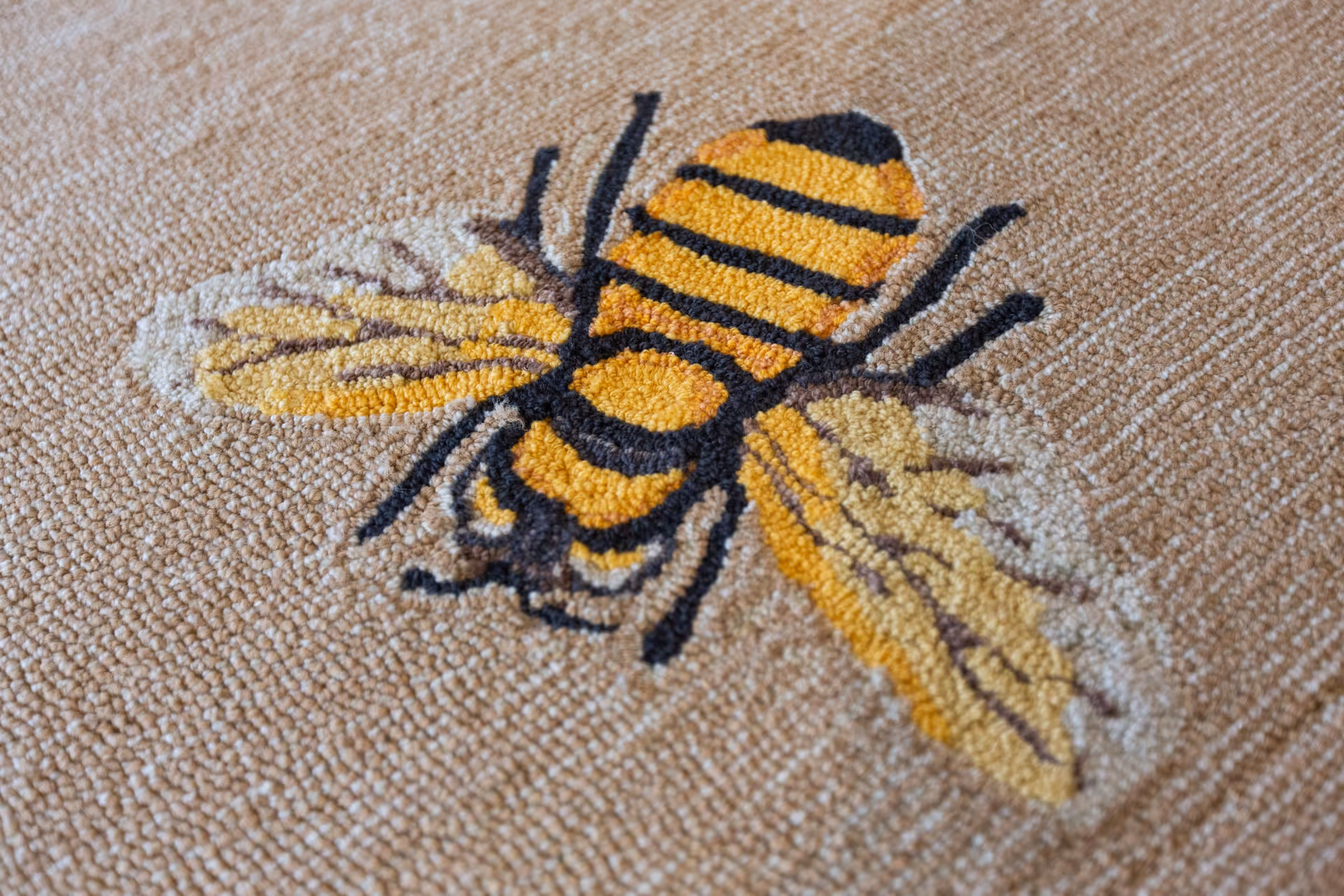 Close-up image of a textured carpet with a detailed design of a yellow and black striped bee with wings.