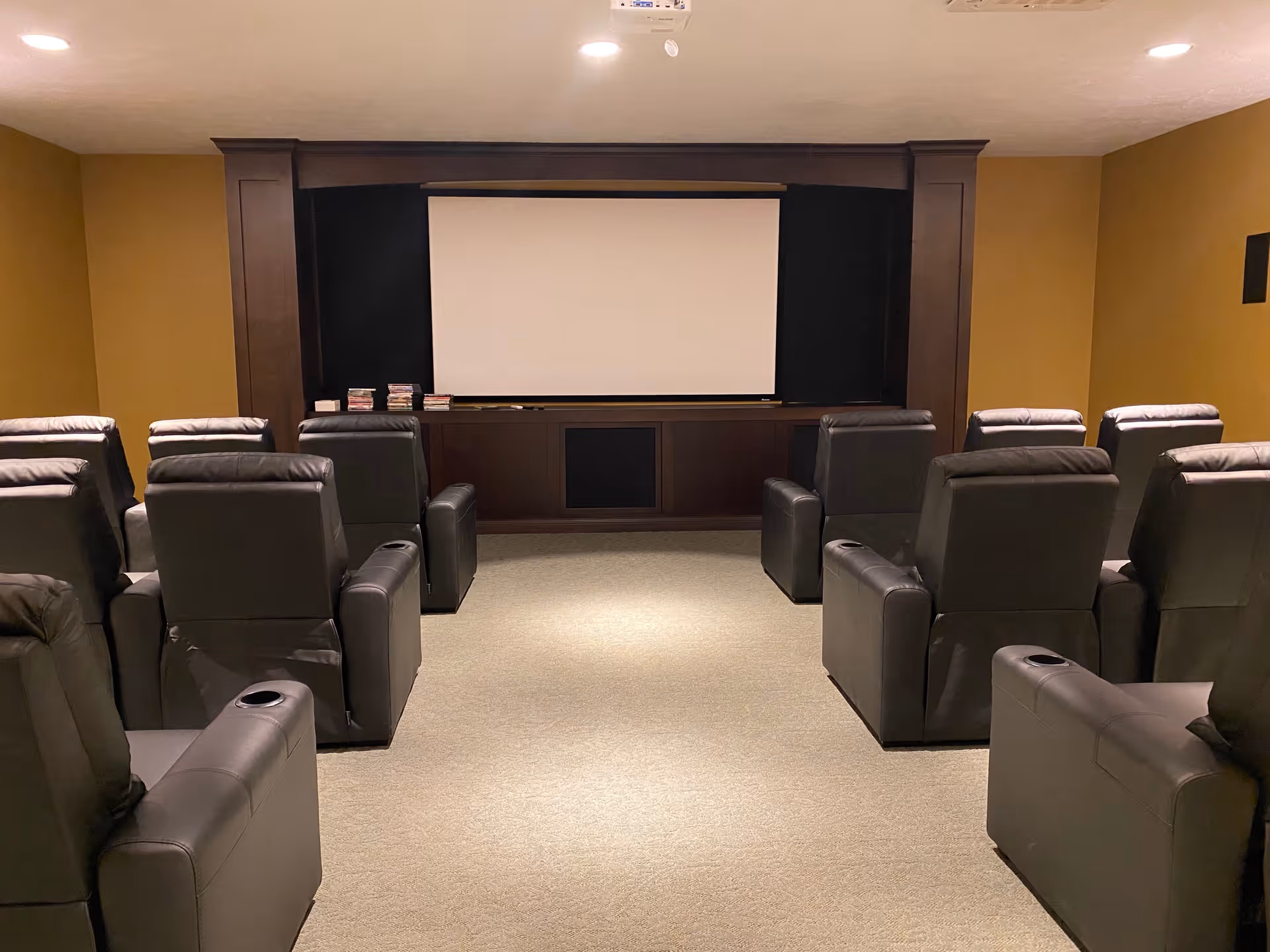 Small private theater room with rows of black leather recliners facing a blank projector screen.