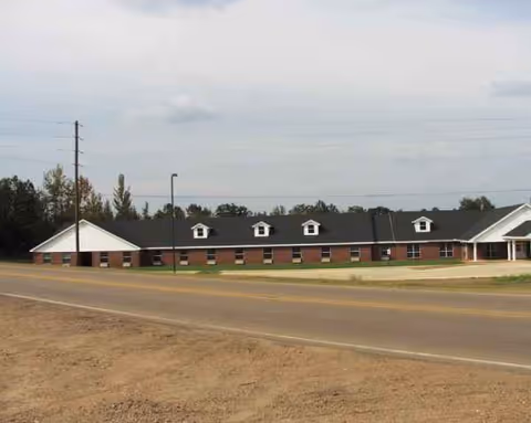 Single-story brick senior living facility along a road with small dormer windows.