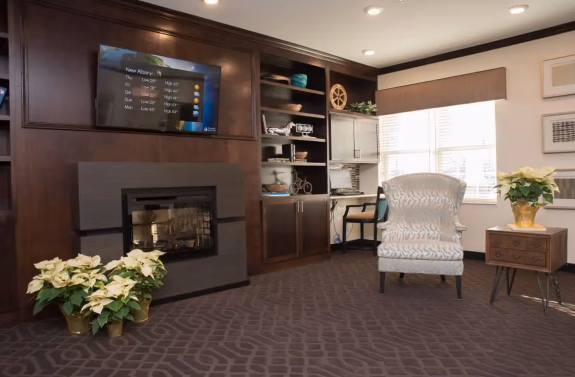 Cozy lounge area with a fireplace and dark wood built-ins, a patterned armchair, side table with a plant, and a wall-mounted TV.
