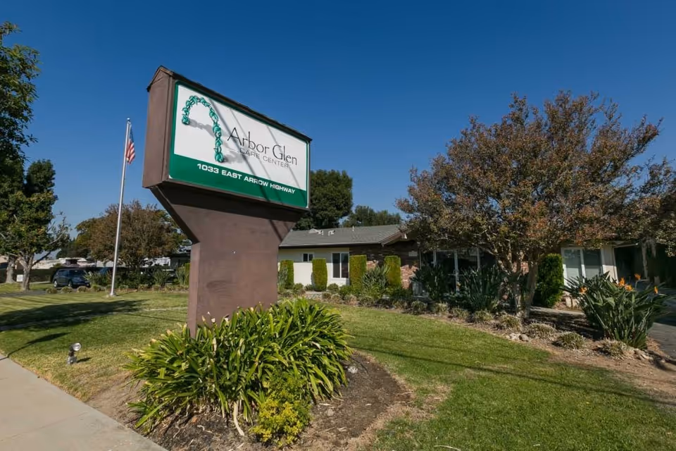 Front lawn and sign reading "Arbor Glen Care Center" in front of a single‑story building under a clear blue sky.