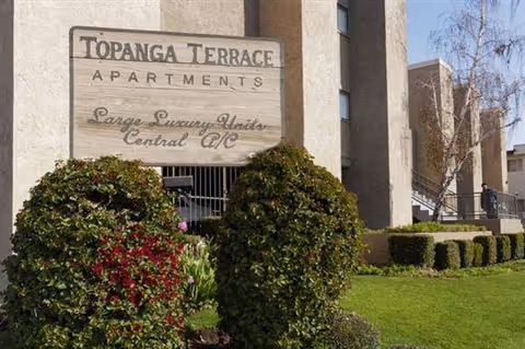 Front exterior of Topanga Terrace building with sign and well-kept shrubs.