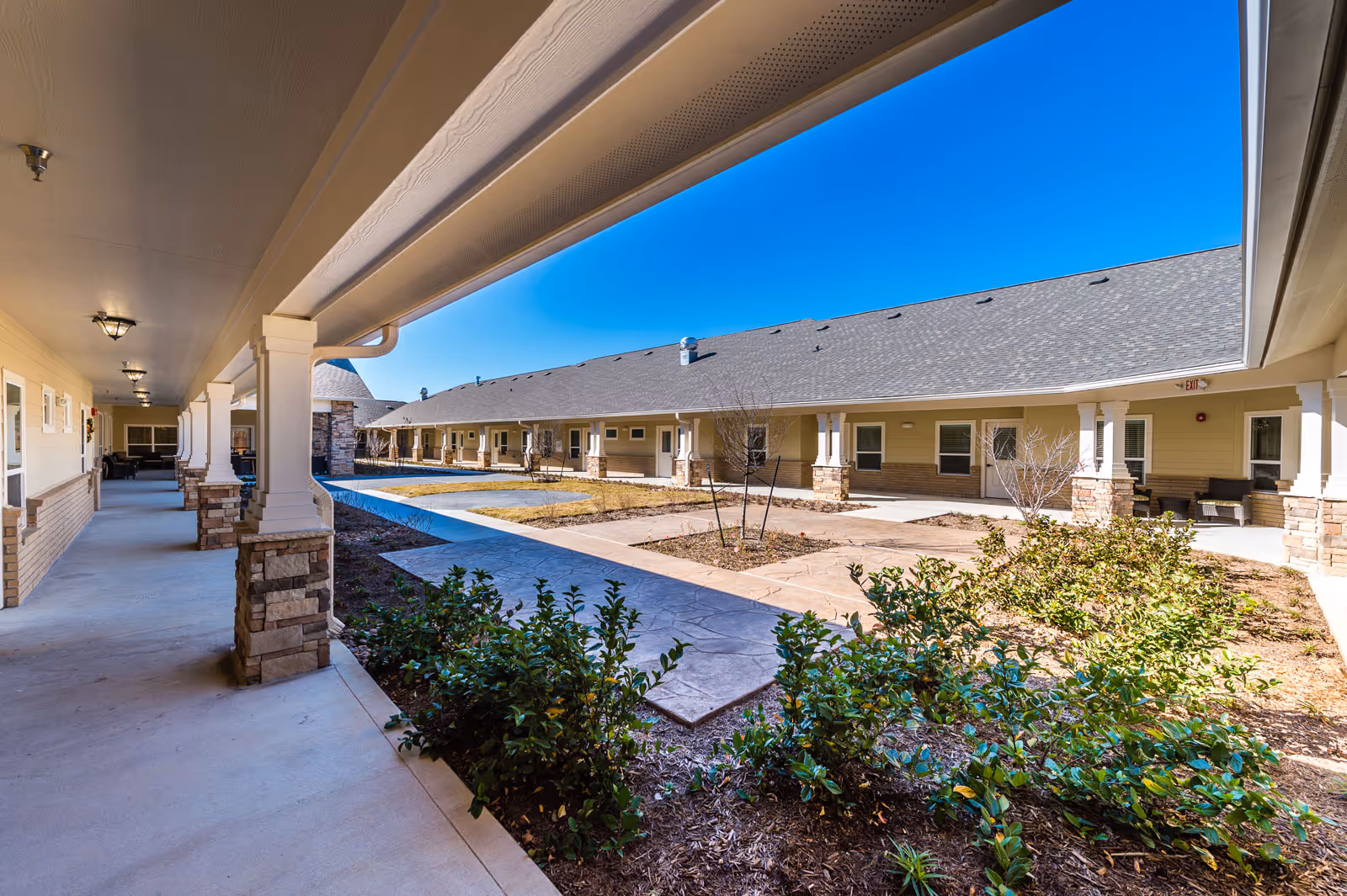 A covered walkway surrounds a courtyard with shrubs and planters at Bristol Park at Cypress.