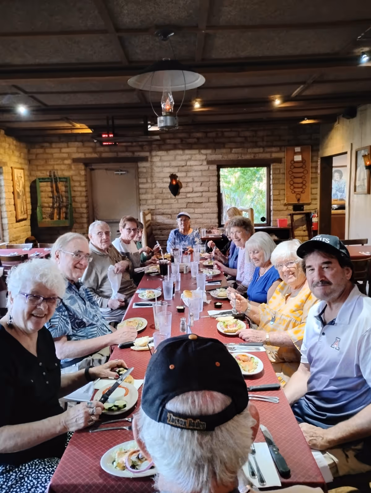 Seniors gathered around a long table in a cozy, rustic dining room enjoying a meal and smiling.