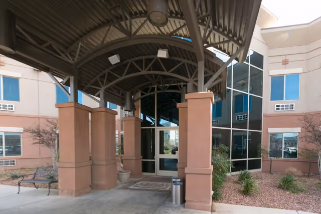 Covered entrance with an arched metal canopy and columns leading to glass double doors at the front of a rehabilitation facility.