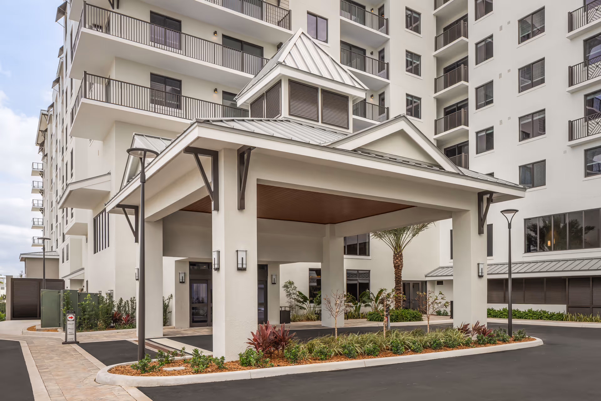 Covered porte-cochere entrance and landscaped driveway in front of a multi-story white apartment building with balconies.