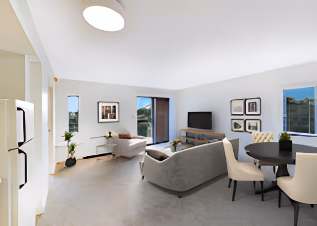 Bright open-plan living room and dining area with gray sofas, a round dining table, and a TV.
