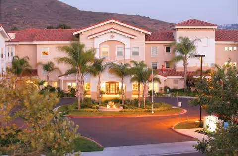 Exterior view of Belmont Village Sabre Springs senior living with palm trees and a curved driveway.