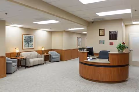 Reception lobby with curved wooden front desk, seating area, lamps, and framed art.