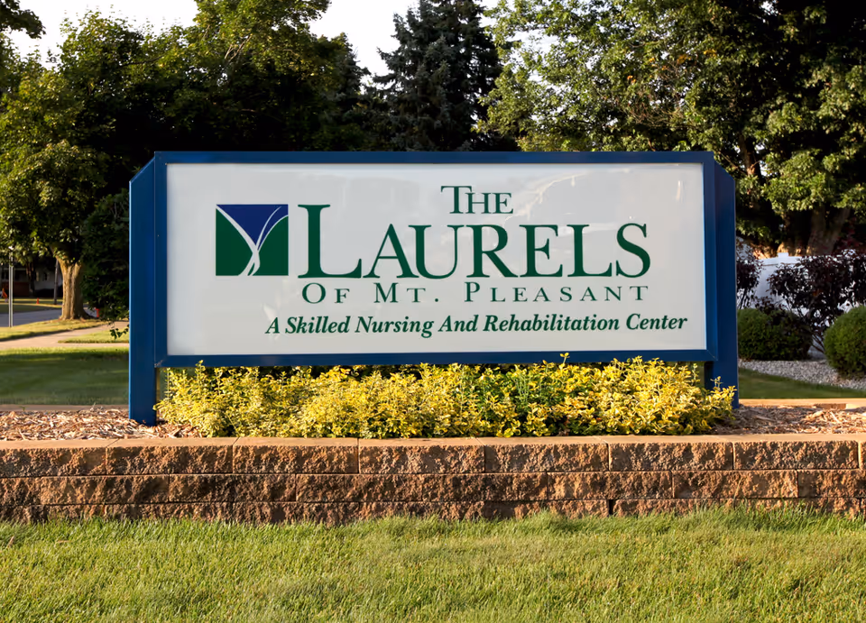 Outdoor sign for The Laurels of Mt. Pleasant, a skilled nursing and rehabilitation center, surrounded by greenery and trees.