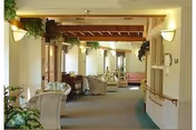 Warm indoor common area with sofas, plants, and wooden beams along a hallway.
