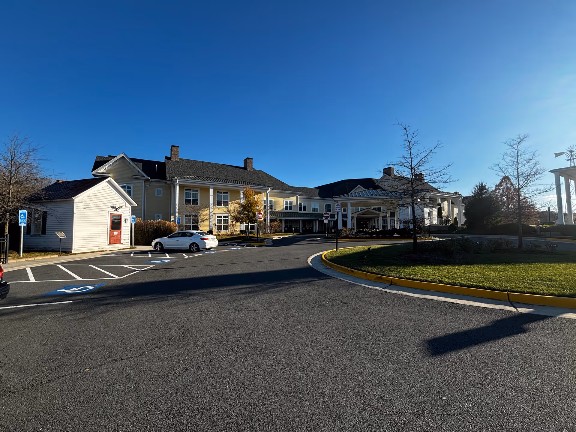 Exterior view of Sunrise at Silas Burke House, a large senior living facility building with a covered entrance, parking spaces including handicapped spots, and a clear blue sky above.