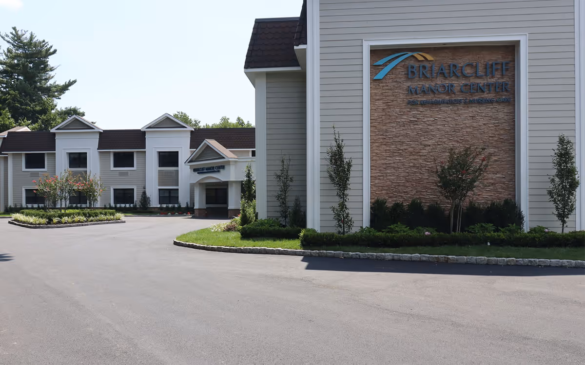 Front entrance and large sign for Briarcliff Manor Center for Rehabilitation and Nursing with a paved driveway and landscaped grounds.