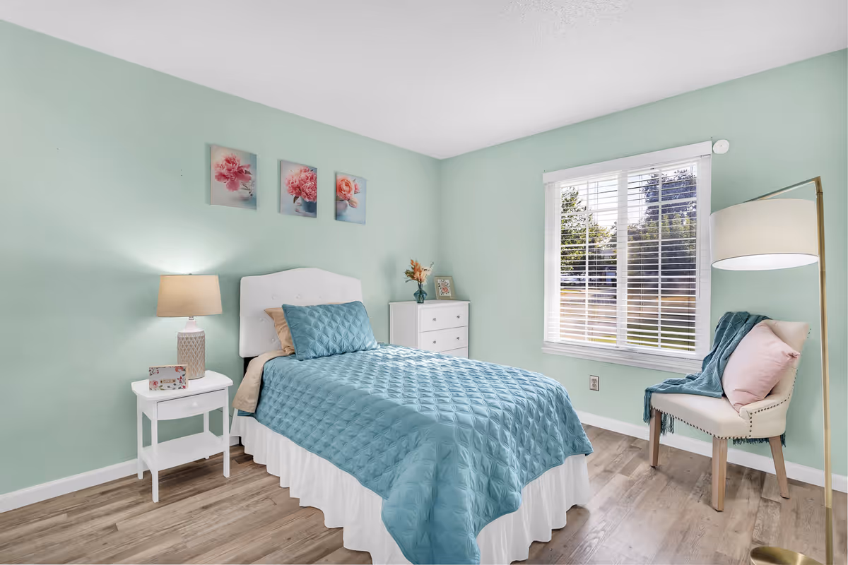 A pastel mint bedroom with a bed, nightstand, dresser, chair, and large window.