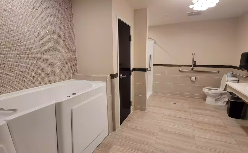 Spacious accessible bathroom with a walk-in tub, roll-in shower, toilet, sink and grab bars.