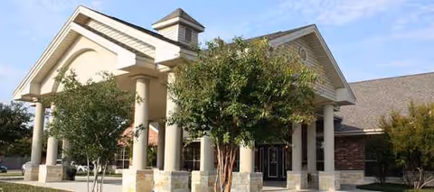 Exterior view of a senior living center with columns and landscaped entrance.