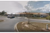 Single-story senior living facility frontage with parking lot, curved driveway, and a small tree.