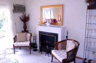 A living room featuring two wicker chairs, a fireplace, and a gold-framed mirror.