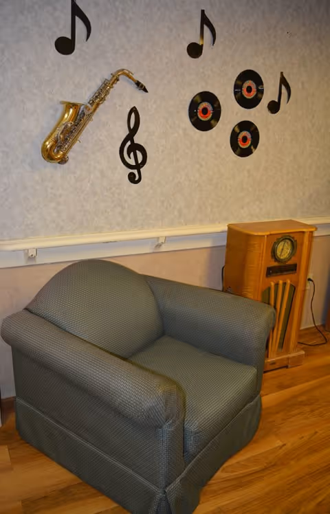 A cushioned armchair sits beside a vintage radio under a wall decorated with musical notes, a saxophone and vinyl records.
