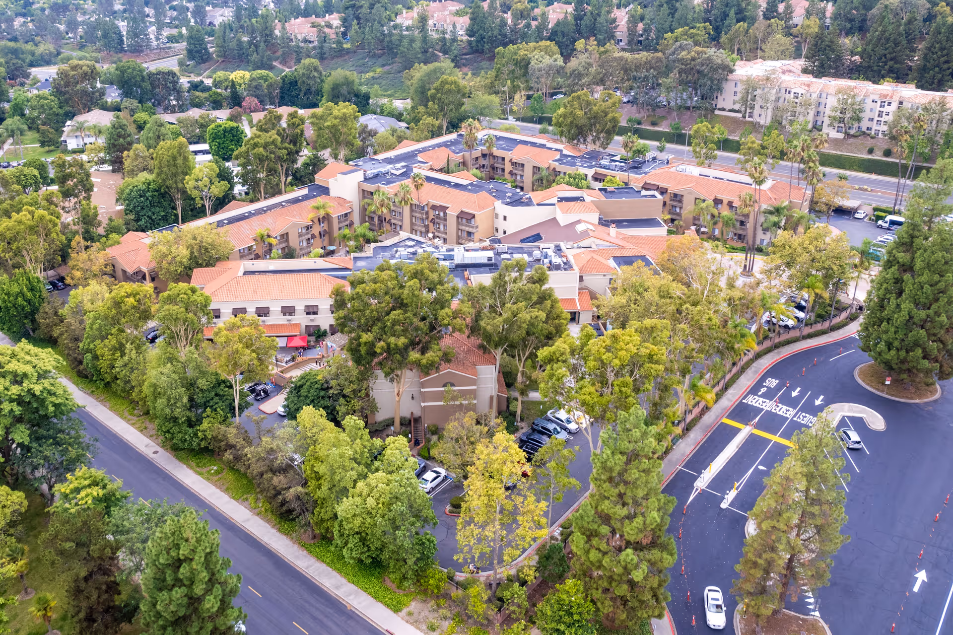 Aerial view of Palm Terrace Healthcare & Rehab Center surrounded by trees and greenery, showing multiple buildings with red-tiled roofs, parking areas, and nearby roads.