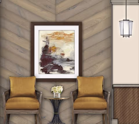Two mustard yellow cushioned chairs with wooden frames are placed side by side against a wall with a chevron wood panel design. Between the chairs is a small round black metal table holding a small vase with white flowers. Above the table hangs a framed abstract painting with shades of brown, beige, and white. To the right, part of a beige wall and a hanging lantern-style light fixture are visible.