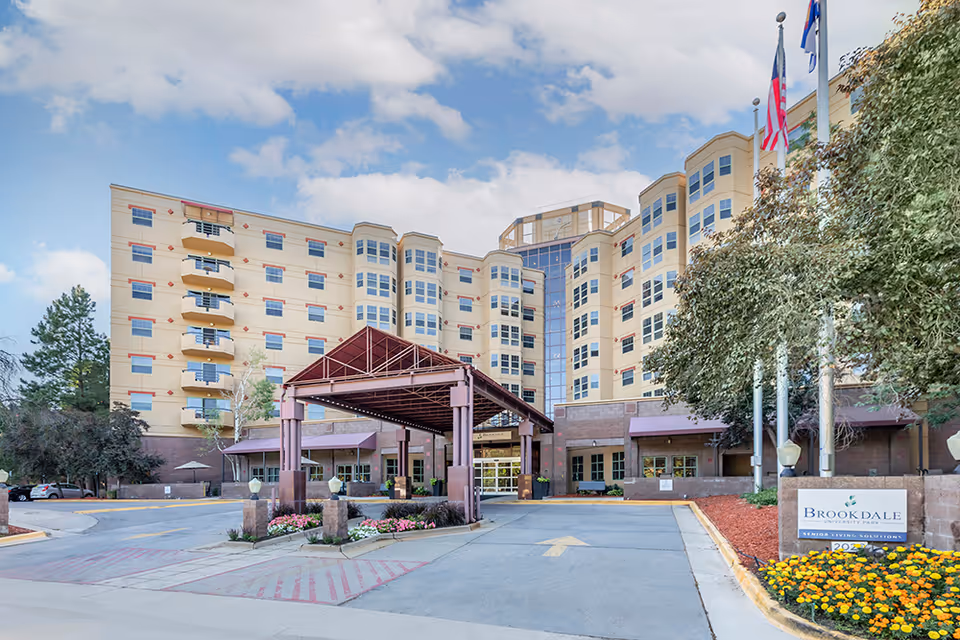 Exterior view of Brookdale University Park with a covered entrance, flags, and landscaped front.